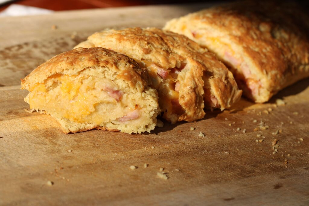 Close up of sandwich roll bread filled ham and cheese cut into rounds sitting on a wooden cutting board.
