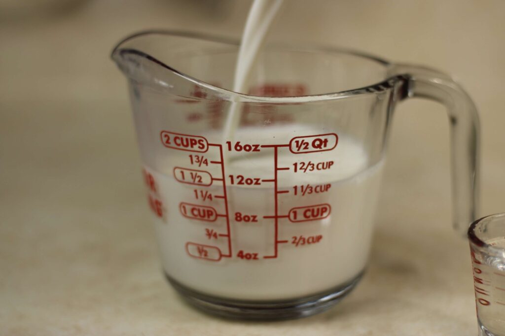 measuring cup being filled with milk to make buttermilk substitute