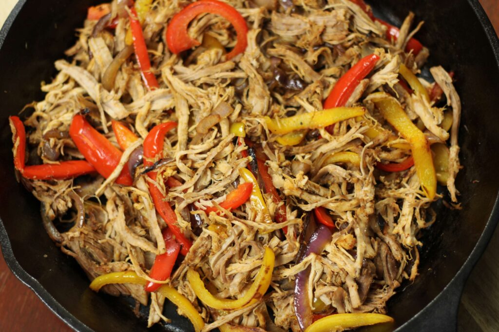 pork carnitas and peppers and onions in cast iron skillet