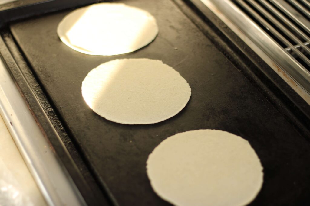 three uncooked corn tortillas on black griddle