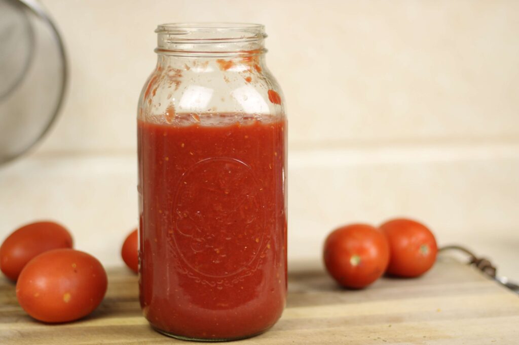 half gallon mason jar of tomato sauce surrounded by Roma tomatoes