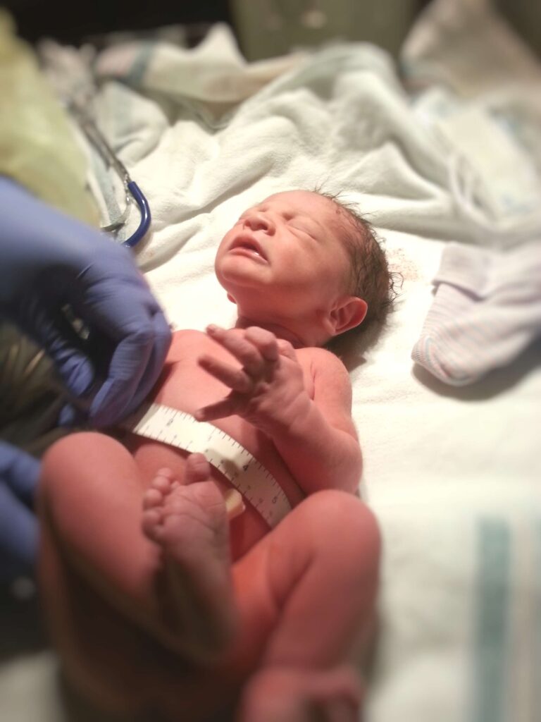 hands measuring newborn's abdomen with tape measure 