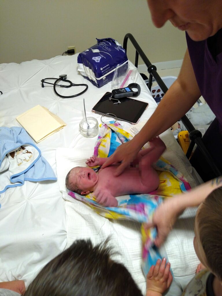 midwife performing newborn exam in bed after natural birth 