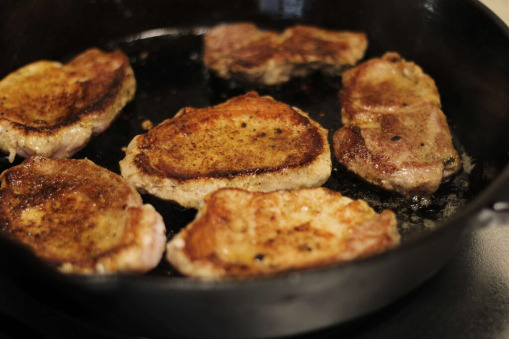 pork chops being cooked in cast iron skillet
