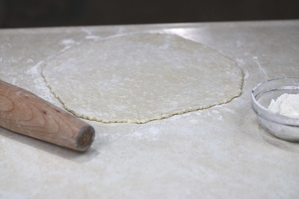 rolled out pie crust next to wooden rolling pin and flour