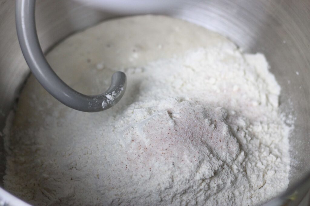 close up of flour and real salt in a bowl of a stand mixer with attachment hook