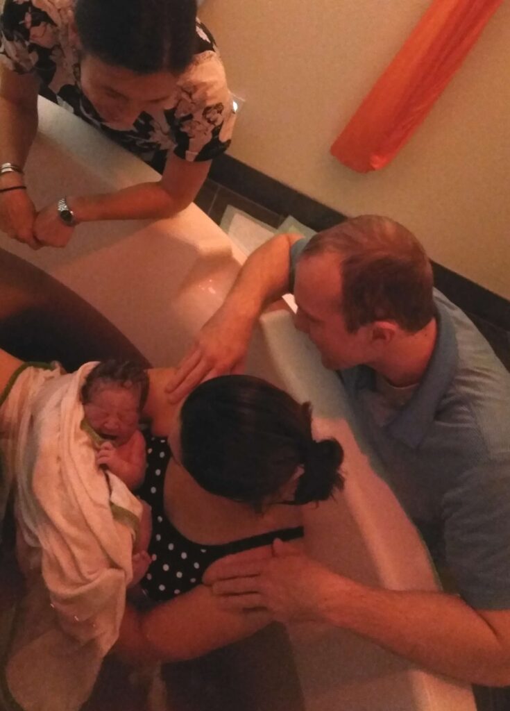 woman in birthing tub holding newborn with dimmed lights as part of a natural birth 