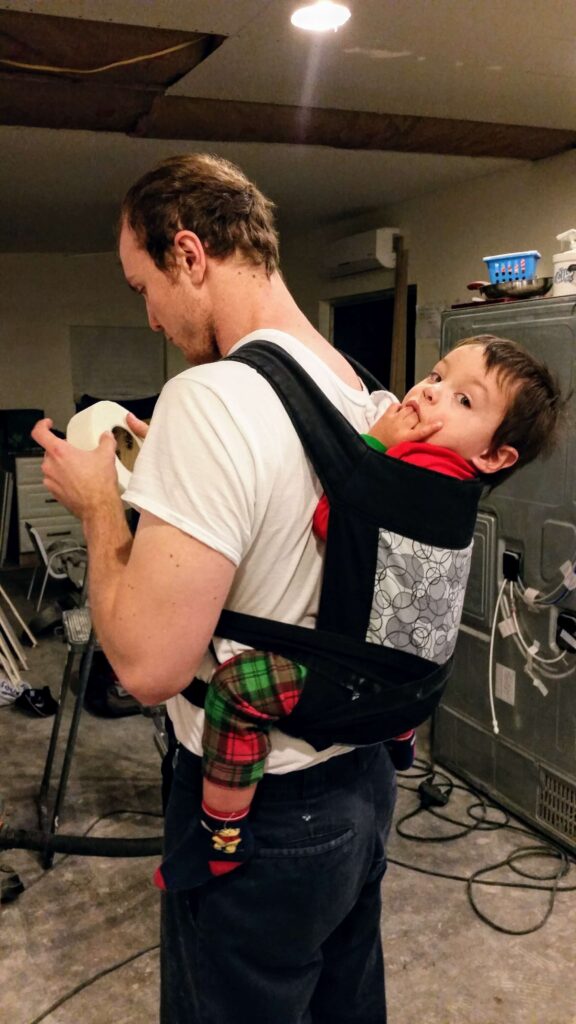 dad wearing toddler in baby wrap while remodeling house