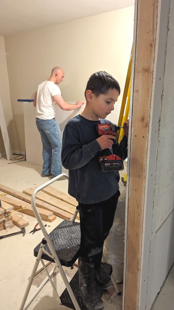 boy helping dad hang drywall in remodeling with kids
