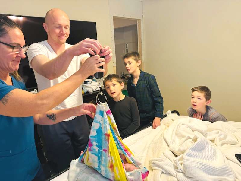 midwife weighting newborn father and brothers watching