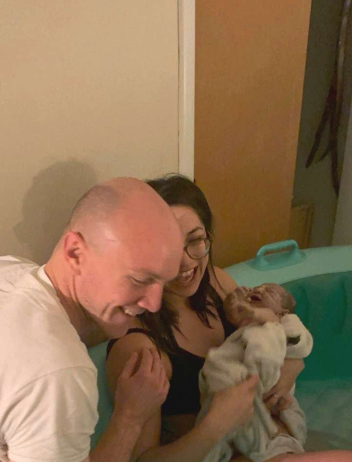 man and woman holding newborn in birthing tub