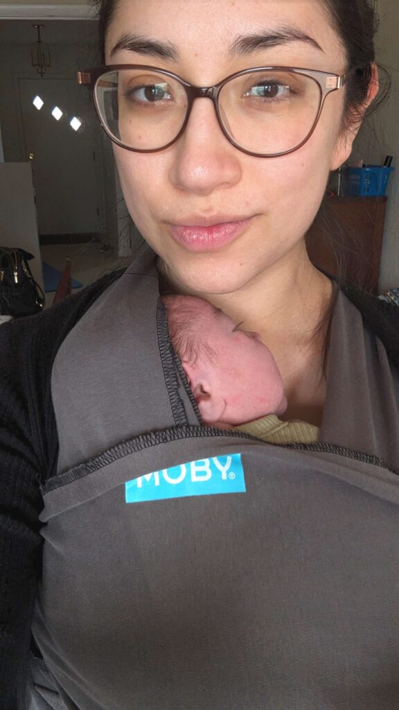 woman with glasses wearing a newborn in a  gray moby wrap 