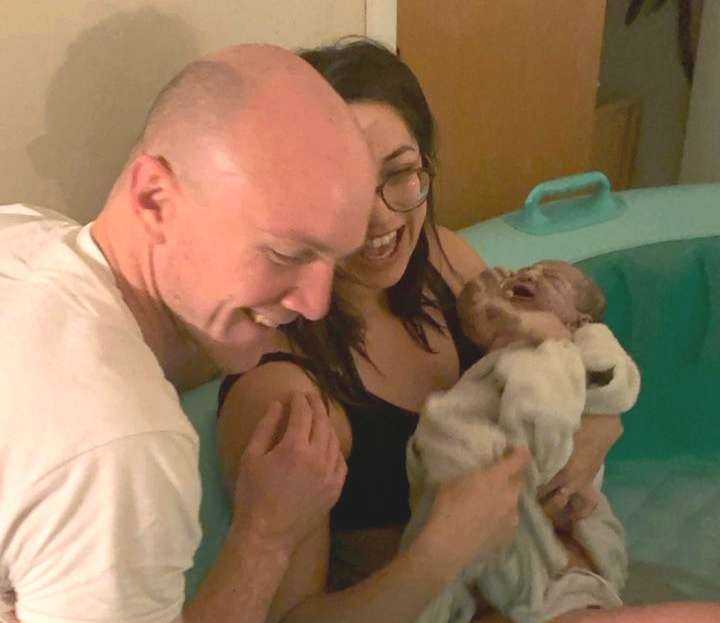 happy dad and mom holding newborn infant moments after peaceful birth