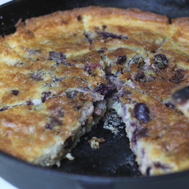 sourdough cherry cobbler in cast iron skillet cut into slices, one slice missing