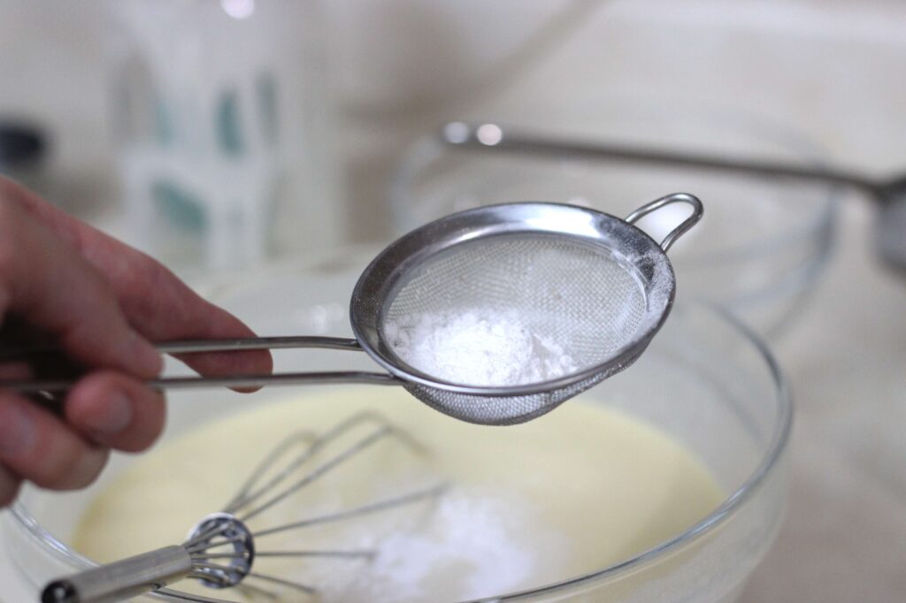 hand holding a sifter with baking soda over cobbler batter 
