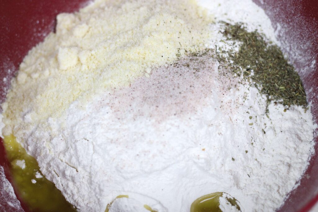 grated parmesan cheese, flour, herbs, olive oil, and sourdough starter in a bowl