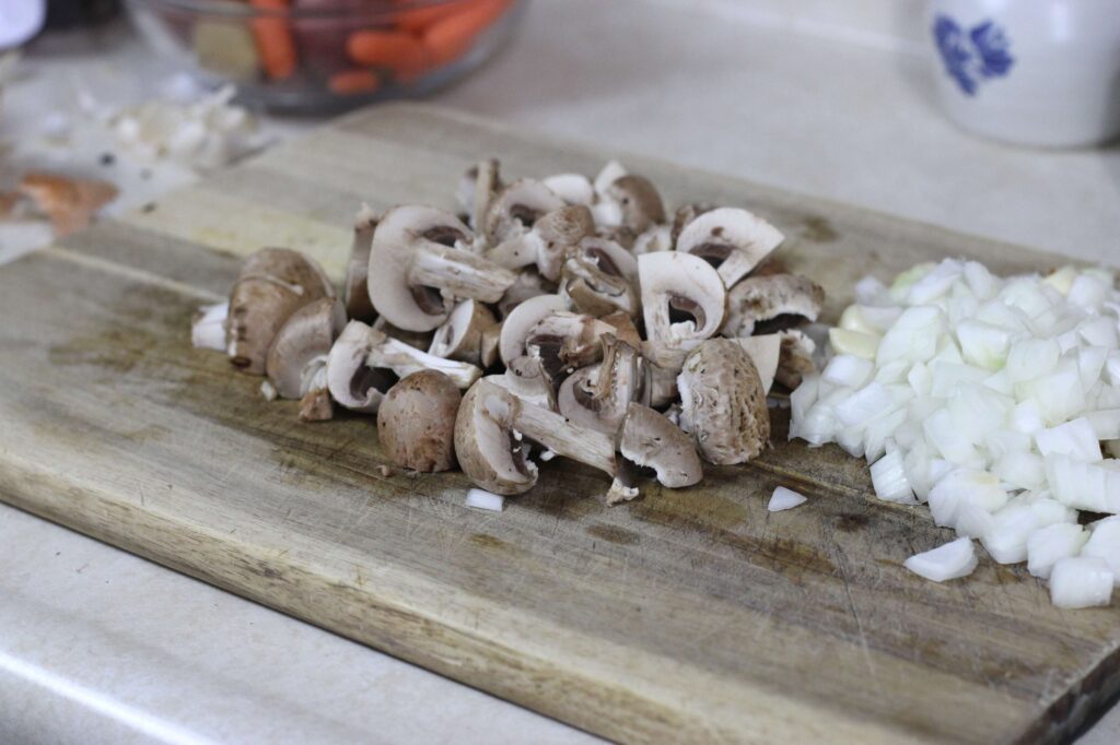 baby portabello mushrooms quartered, diced onion, and garlic cloves on cutting board