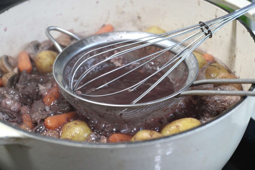 adding flour to thicken stew using a whisk and sifter 
