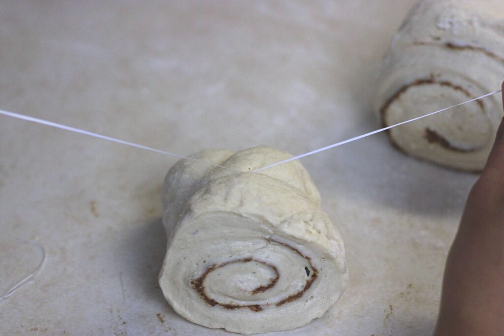 uncooked cinnamon roll being cut by a dental floss 